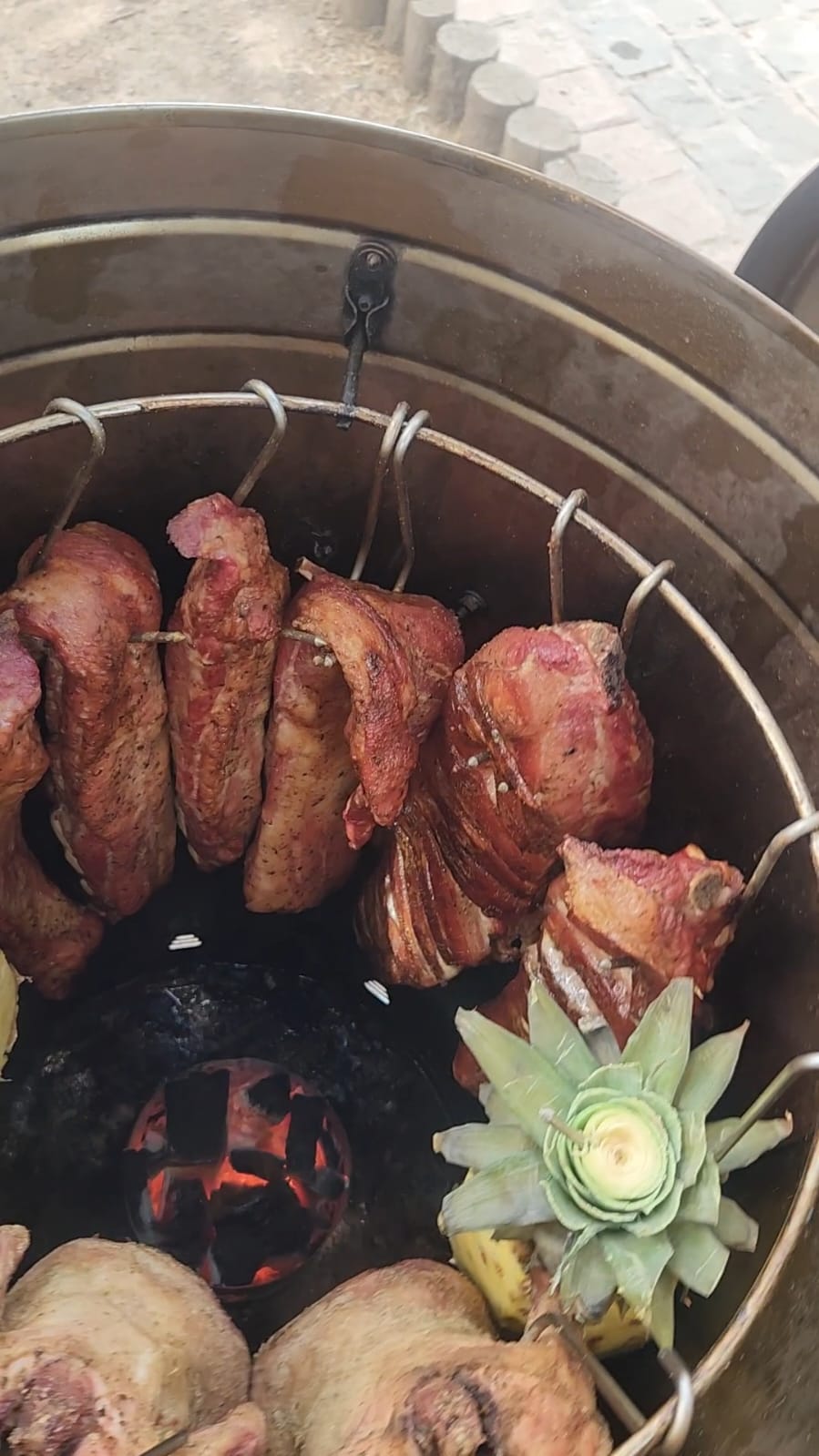 Interior del barril con carnes colgando sobre las brasas y piña